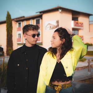 man with sunglasses holding woman in yellow jacket