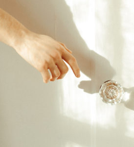 Hand reaching to grab a vintage crystal doorknob to open the door, promoting yes no maybe list.