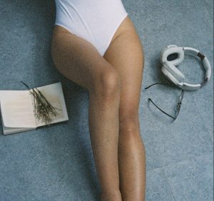 woman in white one piece bathing suit bottom half next to headphones listening to audio erotica