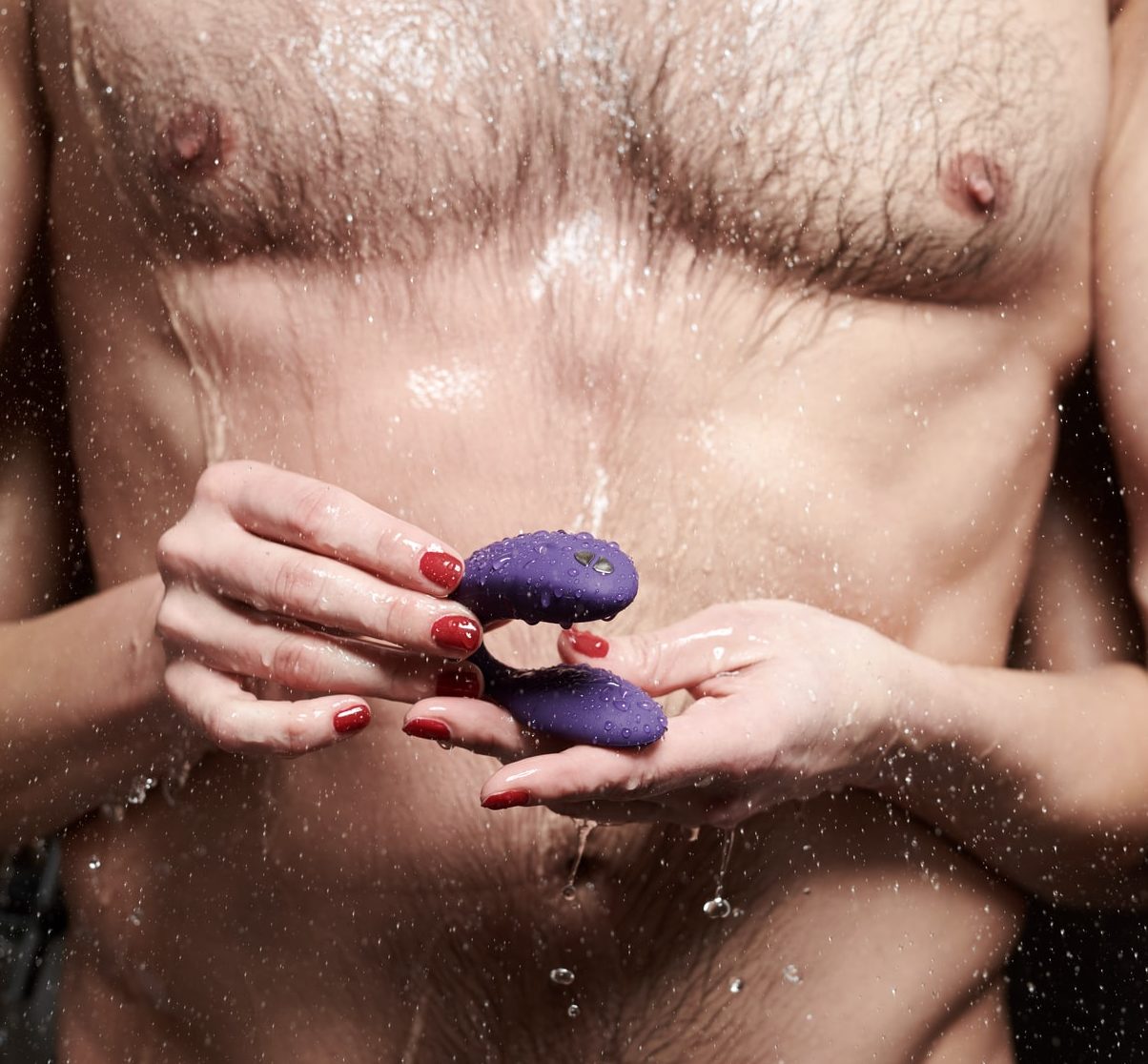 woman holding sex toys for men in front of anonymous man's torso in shower