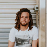 men's health advocate facing camera with white tee shirt and shoulder-length dreadlocks