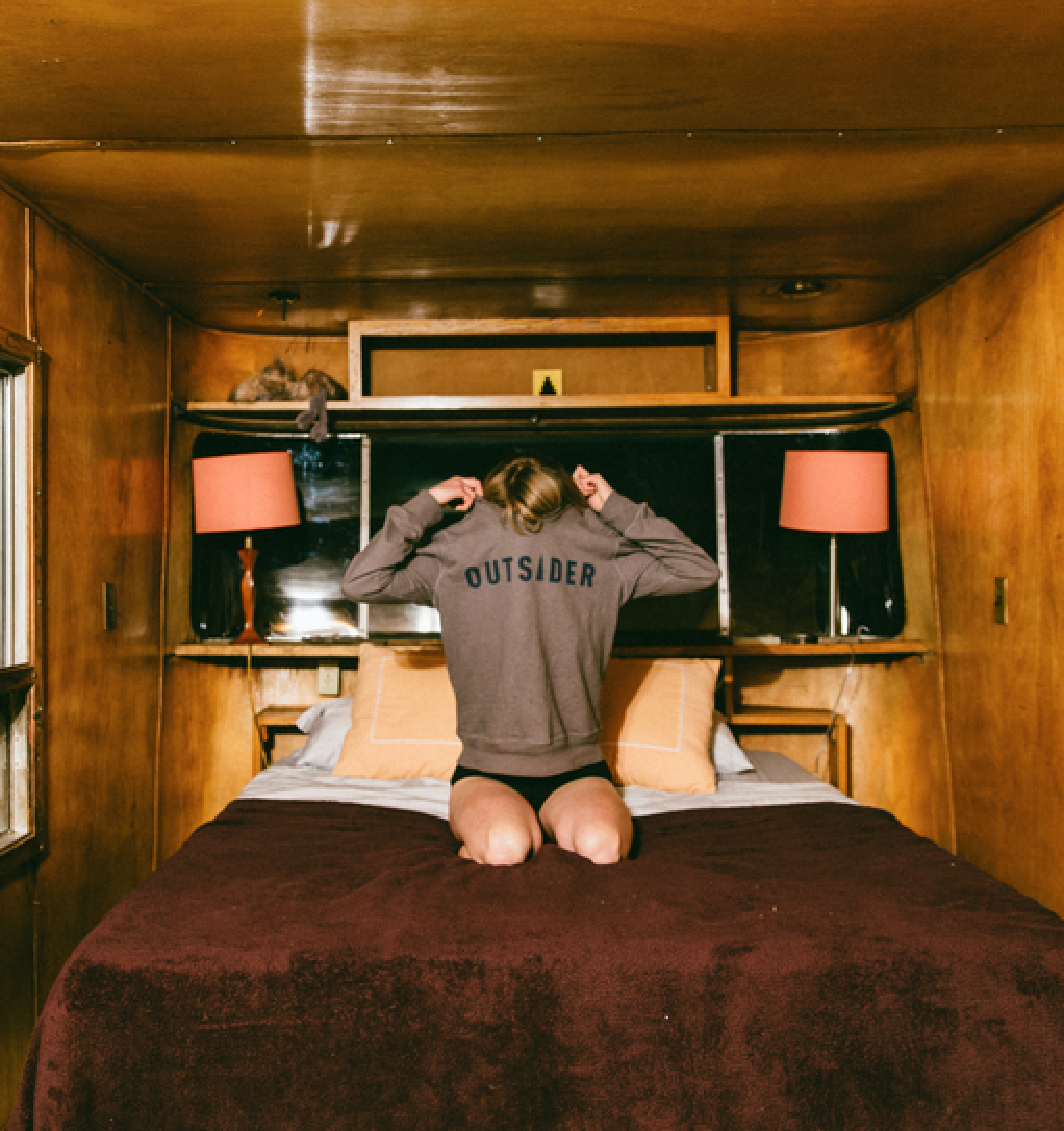 girl sitting on bed taking off sweatshirt