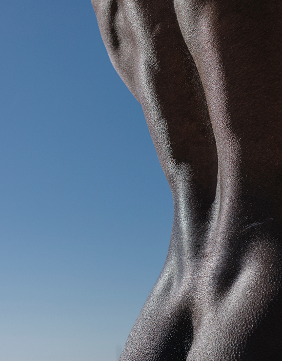Strong back of an athletic African man against a blue sky. Macro photo of black skin texture