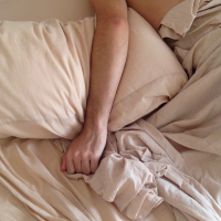 man in beige bed sheets with arm over pilow