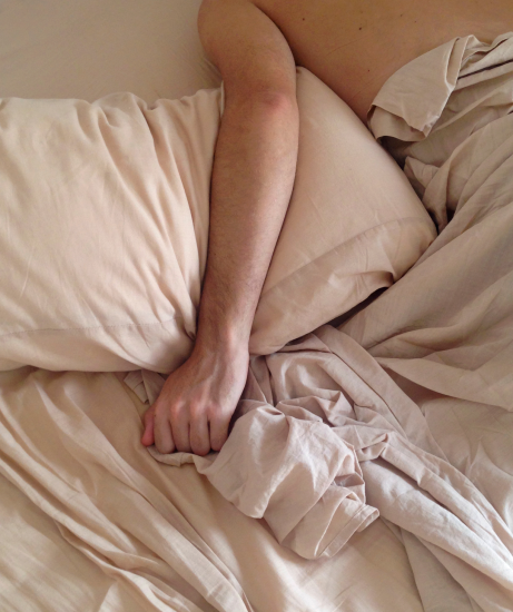 man in beige bed sheets with arm over pilow