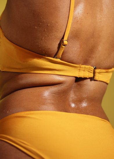 black woman in yellow bikini on curvy body with drops of sweat during summer vacation on hot day.