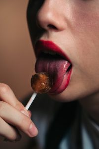 Close up of a sexy woman with red lips licking a lollipop.