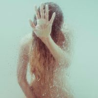 Intimate portrait of an unrecognizable woman masturbating inside the shower and touching the glass with one hand