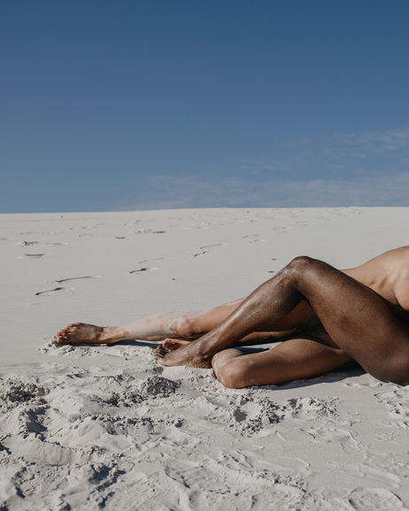 Multiethnic Love couple lying on the sand and hugging. Nude black man and white woman lying on the white sand . Couple in love spending time together in a desert. Horizontal orientation.