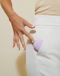 Person putting purple Je Joue Mimi Soft Vibrator into their white pant's pocket