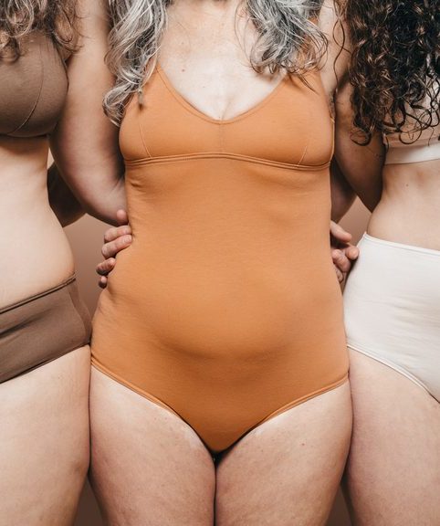 Cropped image of three different ages women embracing each other. They wear underwear which show their normal bodies.