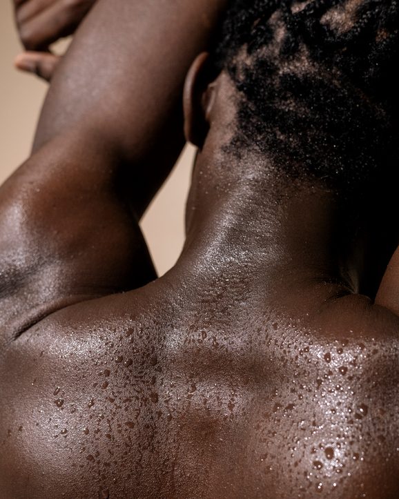 Wet back of a black man, black skin texture with water dripping down his back, close-up