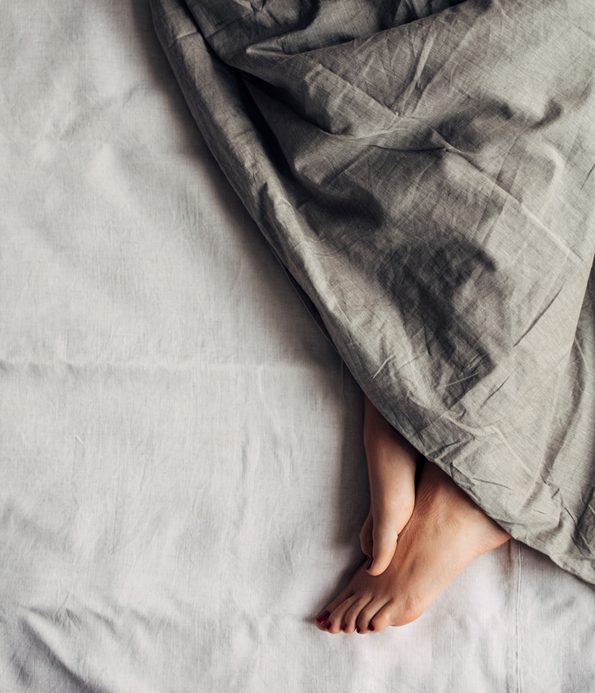 Feet of a woman sleeping under a comforter.