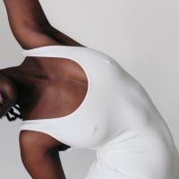 Person in a white ribbed bodysuit stretching gracefully against a neutral background.