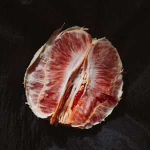 A sliced pink grapefruit resting on dark textured fabric, used as an artistic metaphor for vulva anatomy in an article about the orgasm gap.