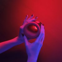 Hands holding the LELO F2S Double Sonic male stroker under red and purple ambient lighting
