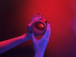 Hands holding the LELO F2S Double Sonic male stroker under red and purple ambient lighting