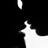 Black and white high-contrast silhouette of two partners leaning in close to touch , illustrating deep sensual connection and decentering penetration.