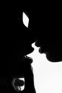 Black and white high-contrast silhouette of two partners leaning in close to touch , illustrating deep sensual connection and decentering penetration.